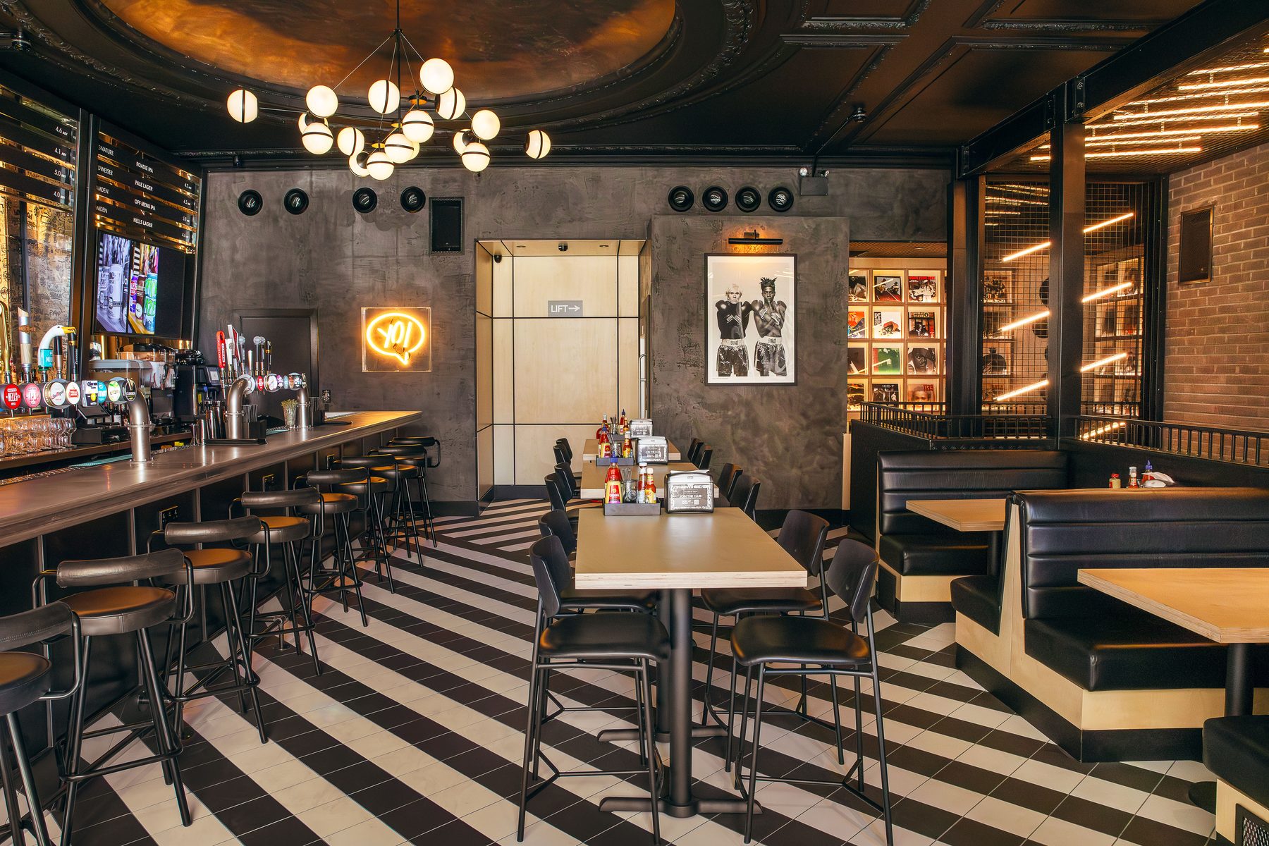 Black Tap, Piccadilly. Bar interior with monochrome striped flooring, dramatic pendant lighting and brass bar fittings.